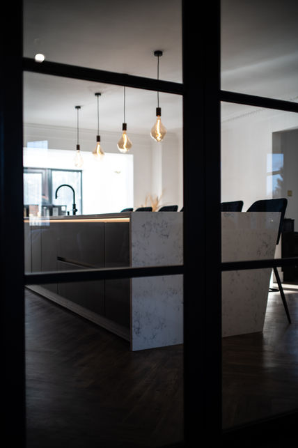 Side view of Next125 NX902 platinum metallic island with angled waterfall end, viewed through a Crittall glass door from the living room in North East UK.