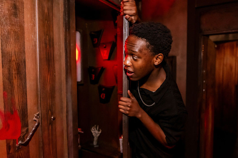 A young man peeping around a door in escape room
