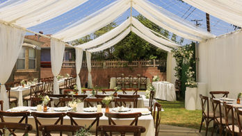 Outdoor wedding reception under an open-sided tent with ivory draping and wooden chairs
