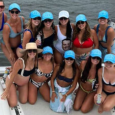 group of women in swimsuits and matching light blue caps smile for a group photo on a catamaran in Fort Lauderdale, Florida, during a bachelorette party. The ocean water is visible in the background