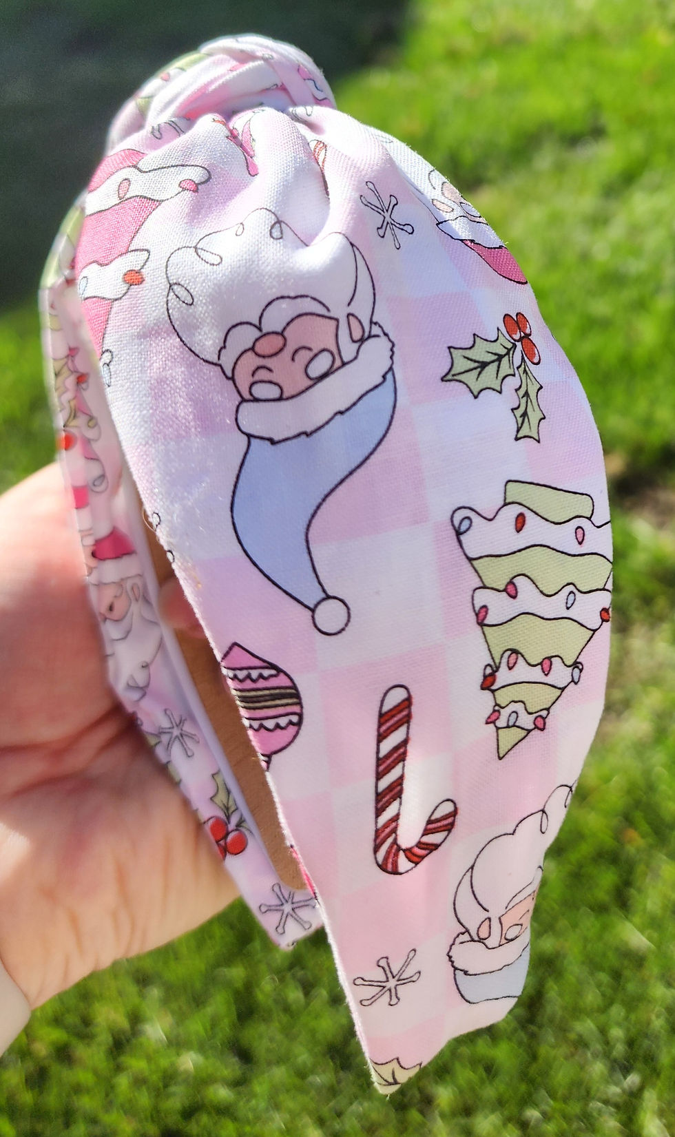 Thumbnail: Hand holding a pink Christmas knotted headband featuring pastel Santa Claus, candy cane, and holiday tree designs