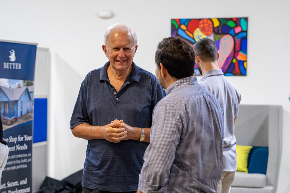 Two men conversing at a networking event with colorful artwork in background.