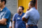 Three men talking outside; person wearing glasses and a blue shirt
