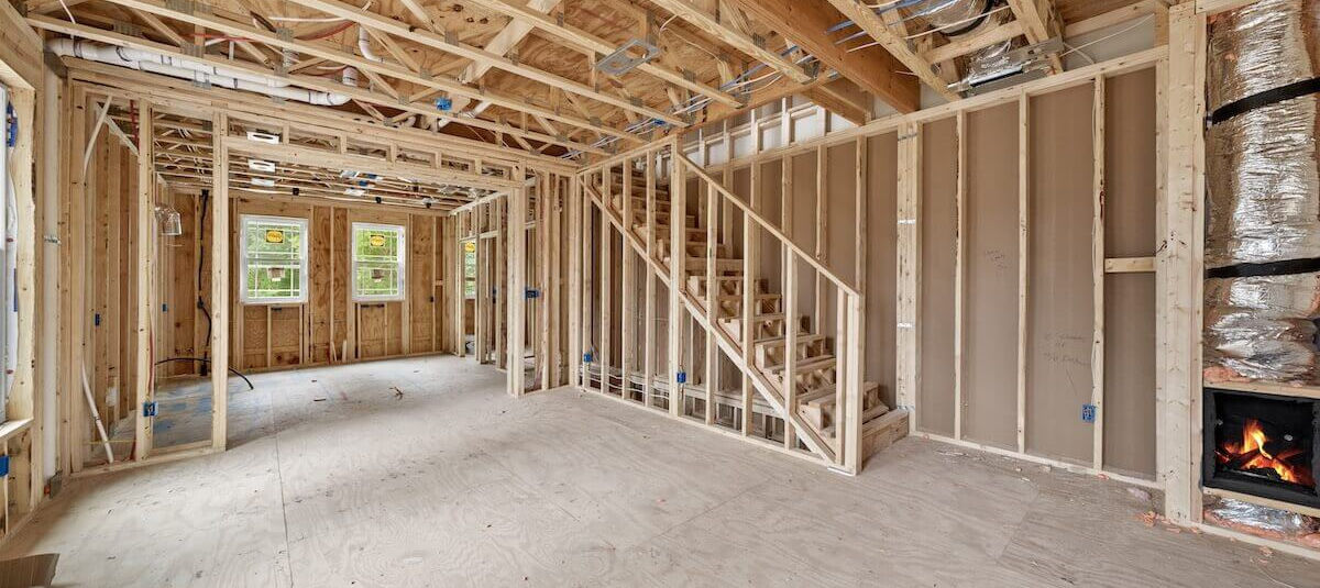 Living room in rough-in stage with windows installed and visible electrical wiring in open framing.