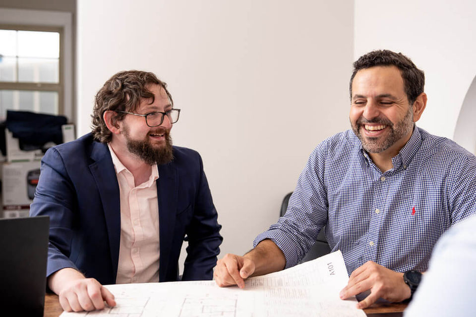 Two men smiling while looking at a document together at a table.