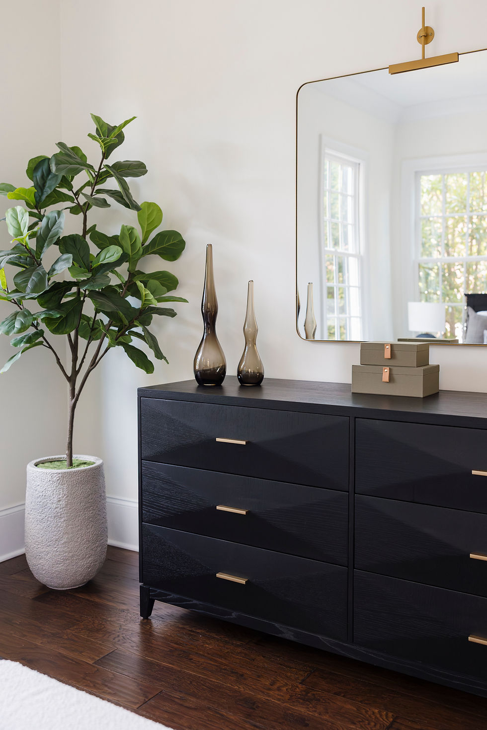 Modern dresser with geometric design and brass handles, topped with tall glass vases and boxes. A potted plant and mirror add elegance.