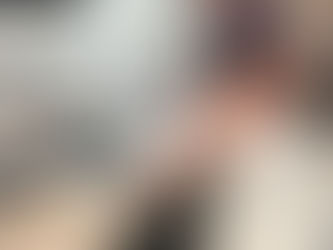 Woman in brown top and white pants examining design samples on a black table. Background has fabric samples, greenery, and a checkered rug.