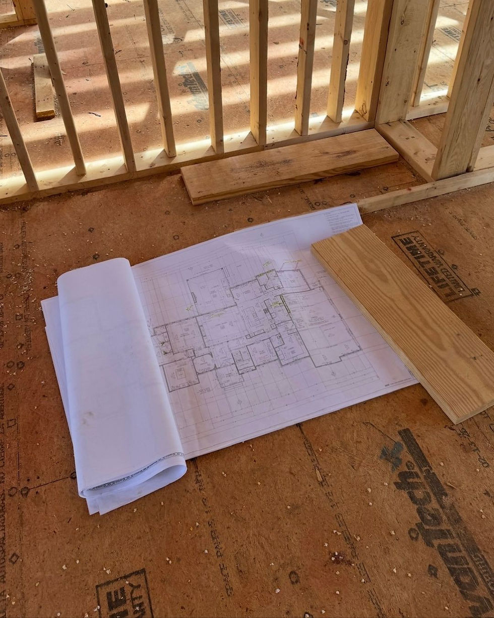 House framing site with a rolled blueprint on subfloor, wood studs and boards in warm sunlight, with Advantech text visible