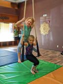 Two happy girls swinging on low trapeze bars above green mats.