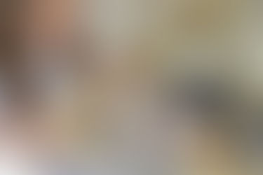 Baby in a wooden swing grips the bar and gazes at a smiling adult in a sensory-rich, child-friendly play area.