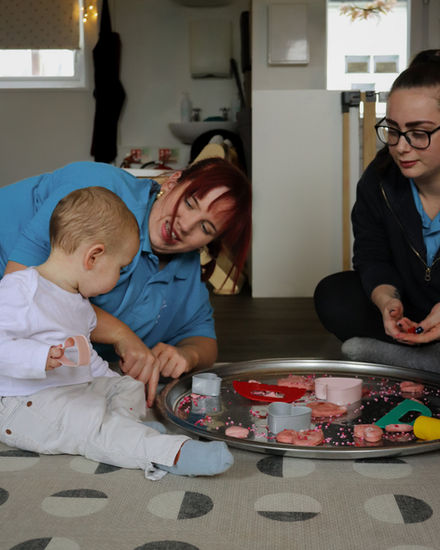 A practitioner shows stretchy dough to a curious toddler, sparking exploration and supporting cognitive development