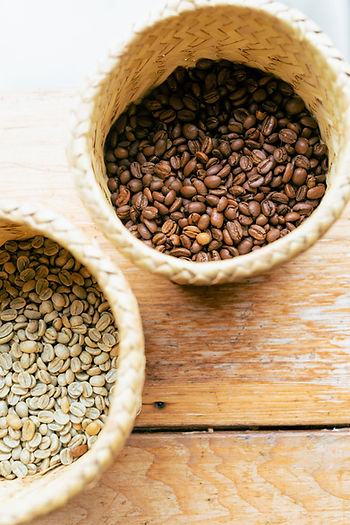 A top-down view of coffee beans transitioning from green to dark roast next to a fresh cup of coffee, illustrating different roast levels.