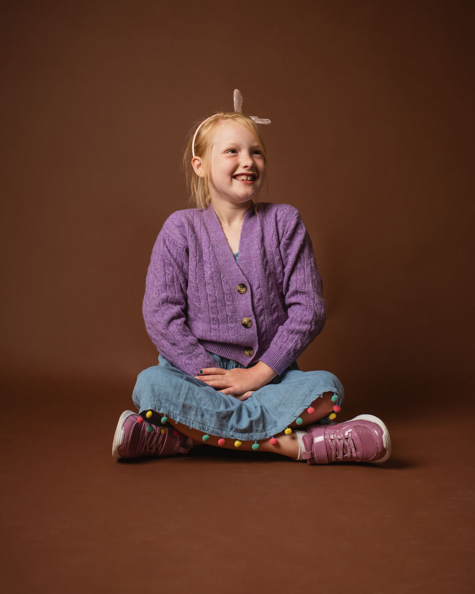 Studio portrait of young girl sitting cross-legged on brown backdrop, Kent
