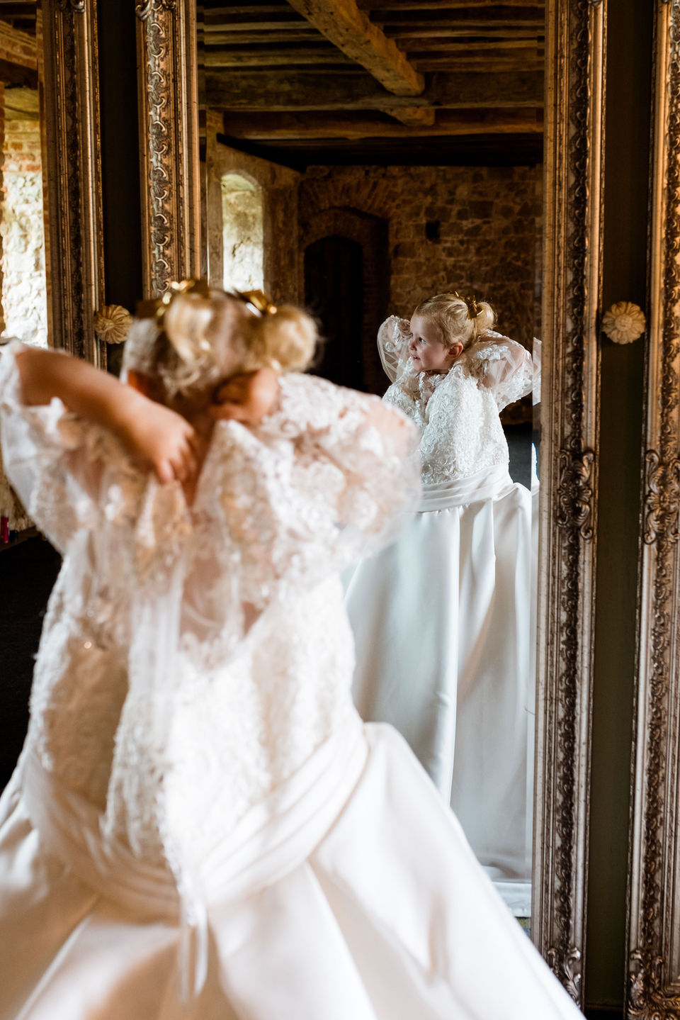 Young bridesmaid tries on mums wedding dress in the mirror on the wedding morning. luxuary wedding photography by Dover Media Group
