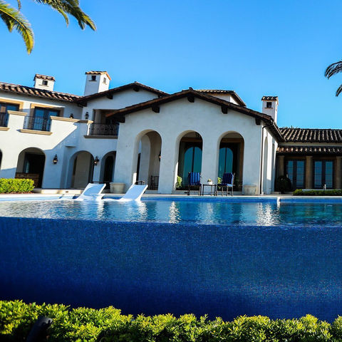 A luxury Mediterranean-style home in Laguna Beach with an infinity pool, arched windows and doors, and submerged lounge chairs, designed by Leli Construction.