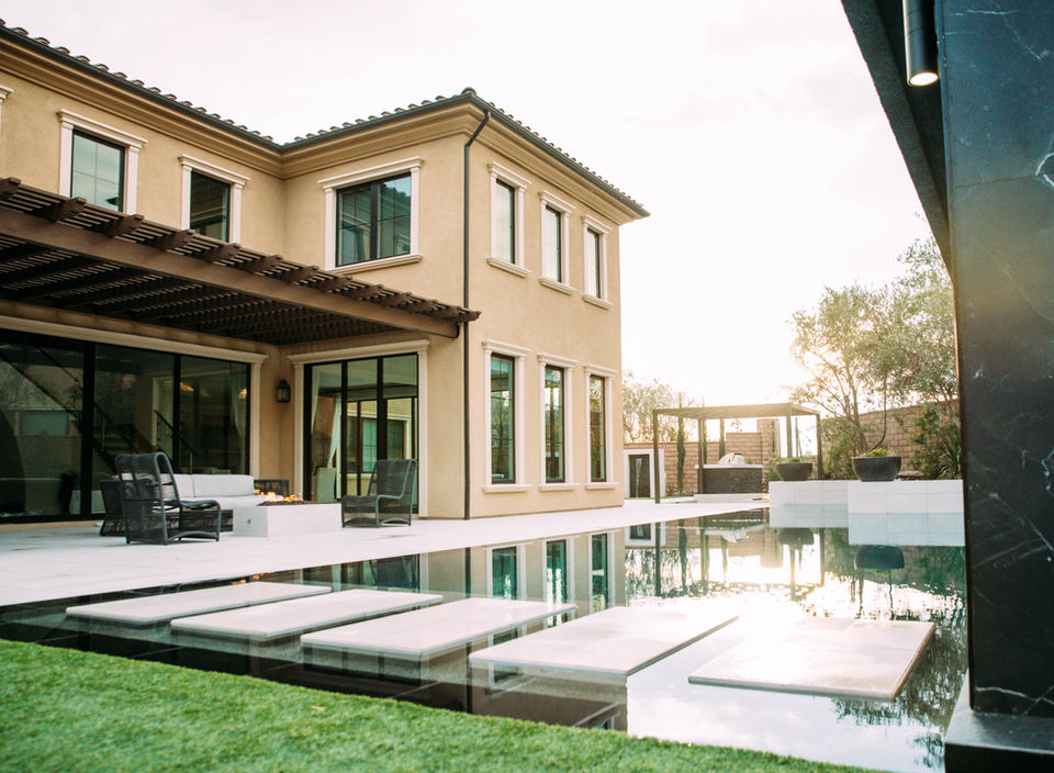 Custom luxury home with floating steps over a reflective pool, large glass doors, and pergola-covered patio designed by Leli Construction in Southern California.