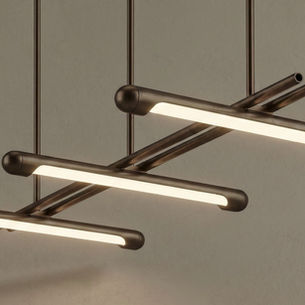 Bronskleurige pendel met drie verspringende lichtbuizen aan dunne stangen voor een grijsgroene wand