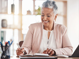 Mature woman with short silver hair smiling while working at a desk in a bright, contemporary setting.