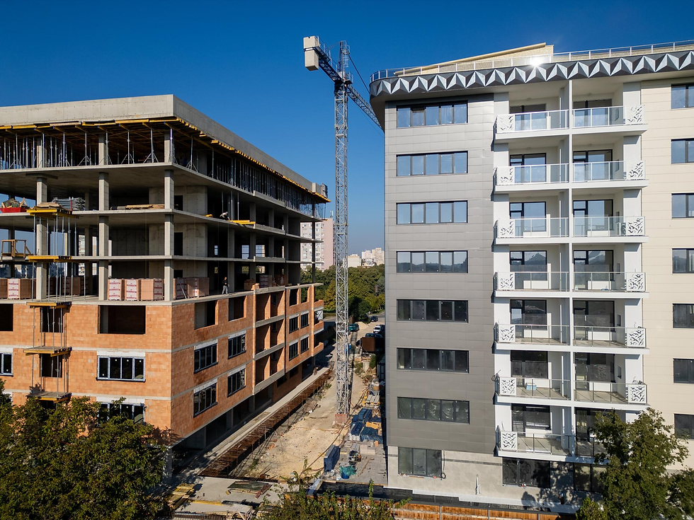 青空の下、左に建設中の中層ビル、右に完成したバルコニー付き集合住宅。中央にタワークレーンが立つ建築現場。
