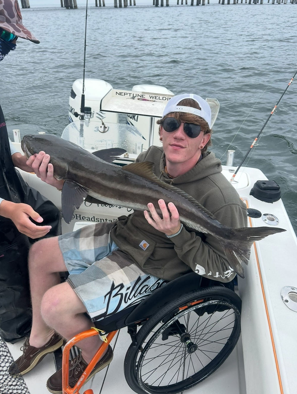 Young man in wheelchair on boat holding fish