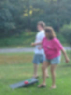 Woman throwing cornhole bag with man watching outdoors