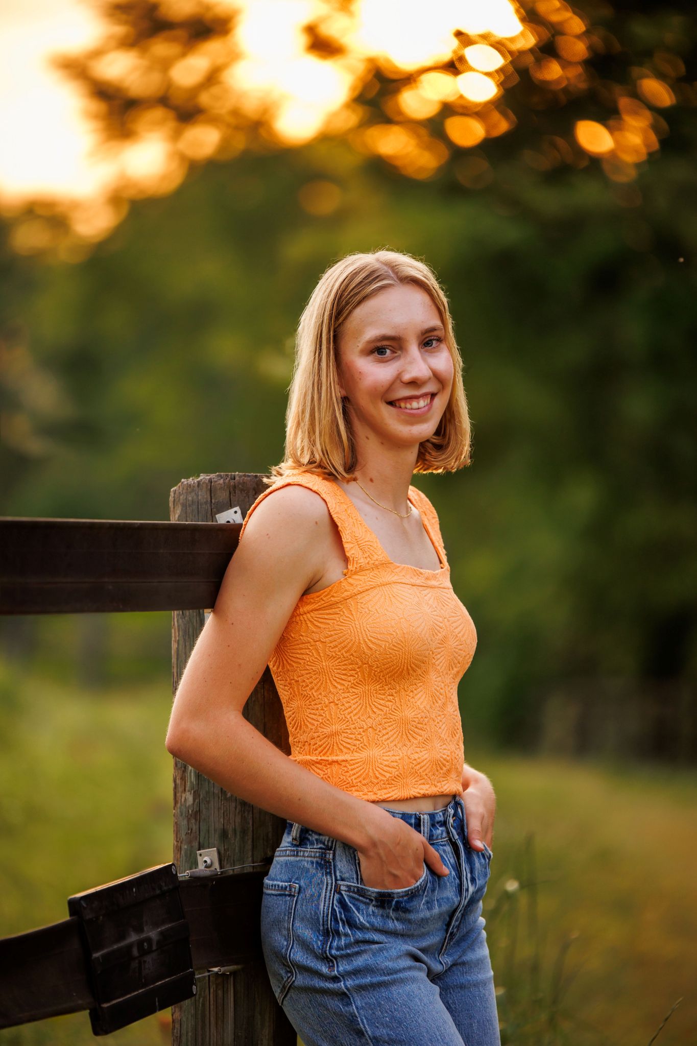 senior portrait of girl leaning on a horse fence at sunset
