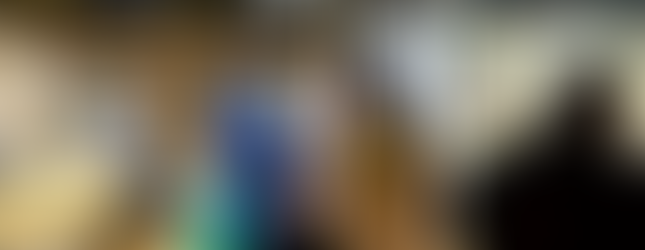 Community members interact inside the museum shop area. A child in a wheelchair draped in a flag is joined by a group of adults in traditional African clothing.