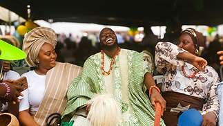 Three people in traditional African clothing laughing together at a cultural celebration.