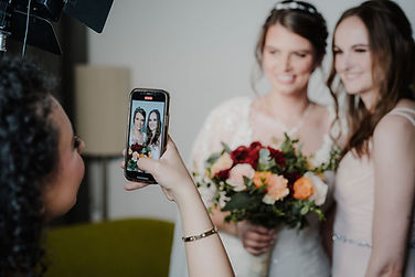 Make-up Artist Manuela Guirguis lächelt und fotografiert eine Braut mit ihrer Trauzeugin am Ende ihres Stylings.