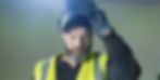 A head and shoulders shot of a bearded man wearing a high visibility jacket about to pull a welding mask over his face.
