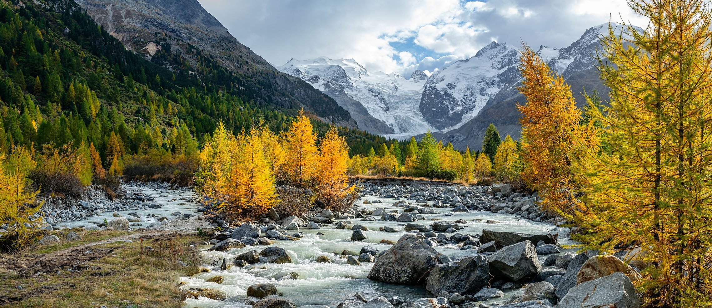 Schmelzwasserfluss durch Gletschertal mit goldenen Lärchen im Herbst