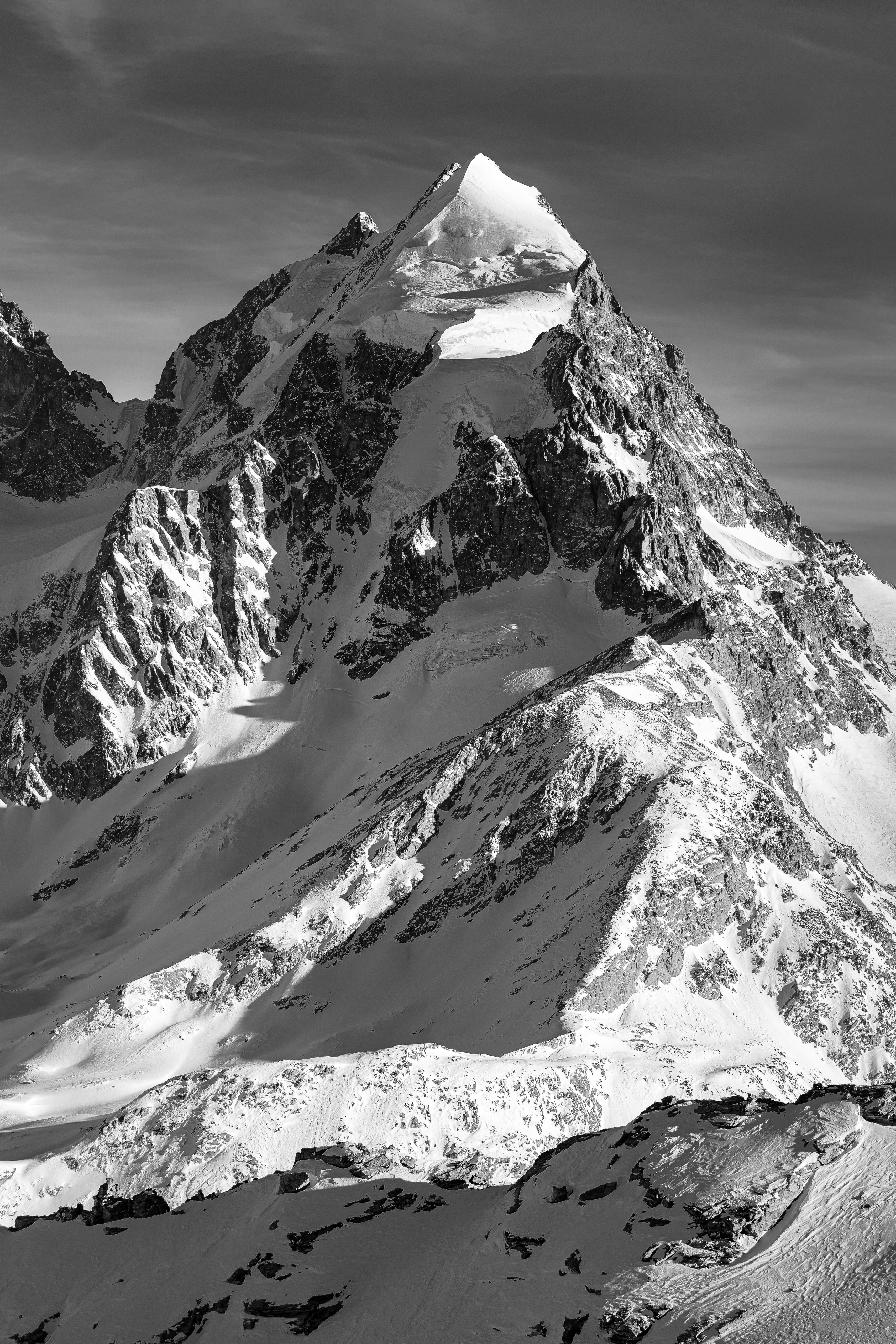 Ein Bergporträt des Piz Roseg im Engadin. Schwarzweiss und Hochformat betonen die markante Gipfelform und die plastischen Strukturen von Fels und Eis.