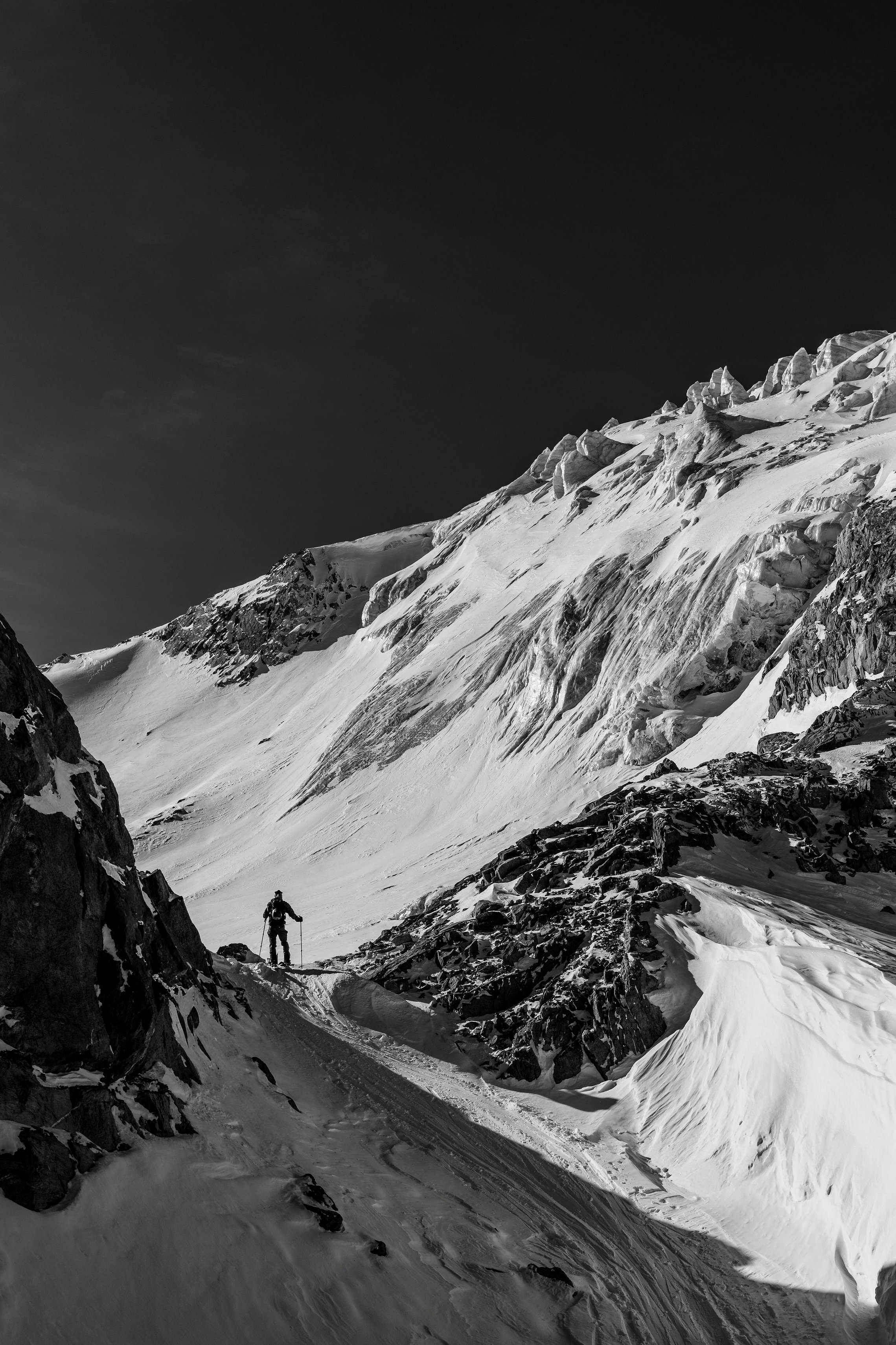 Skitourengänger auf schmalem Grat zwischen Fels, Schnee und Schatten