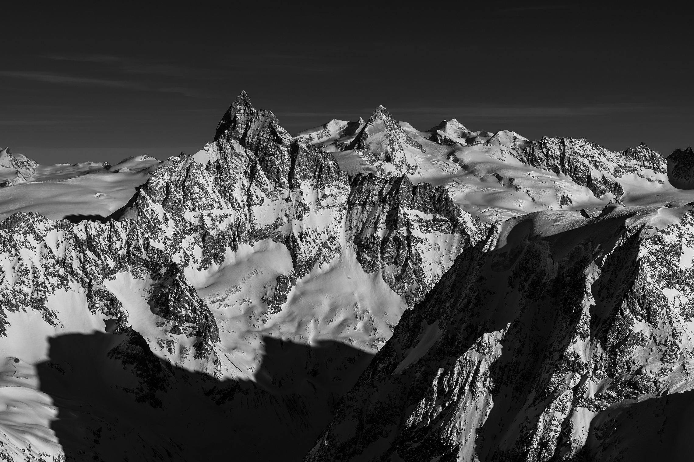 Dunkler Berggrat vor heller Hochgebirgslandschaft mit fernem Matterhorn