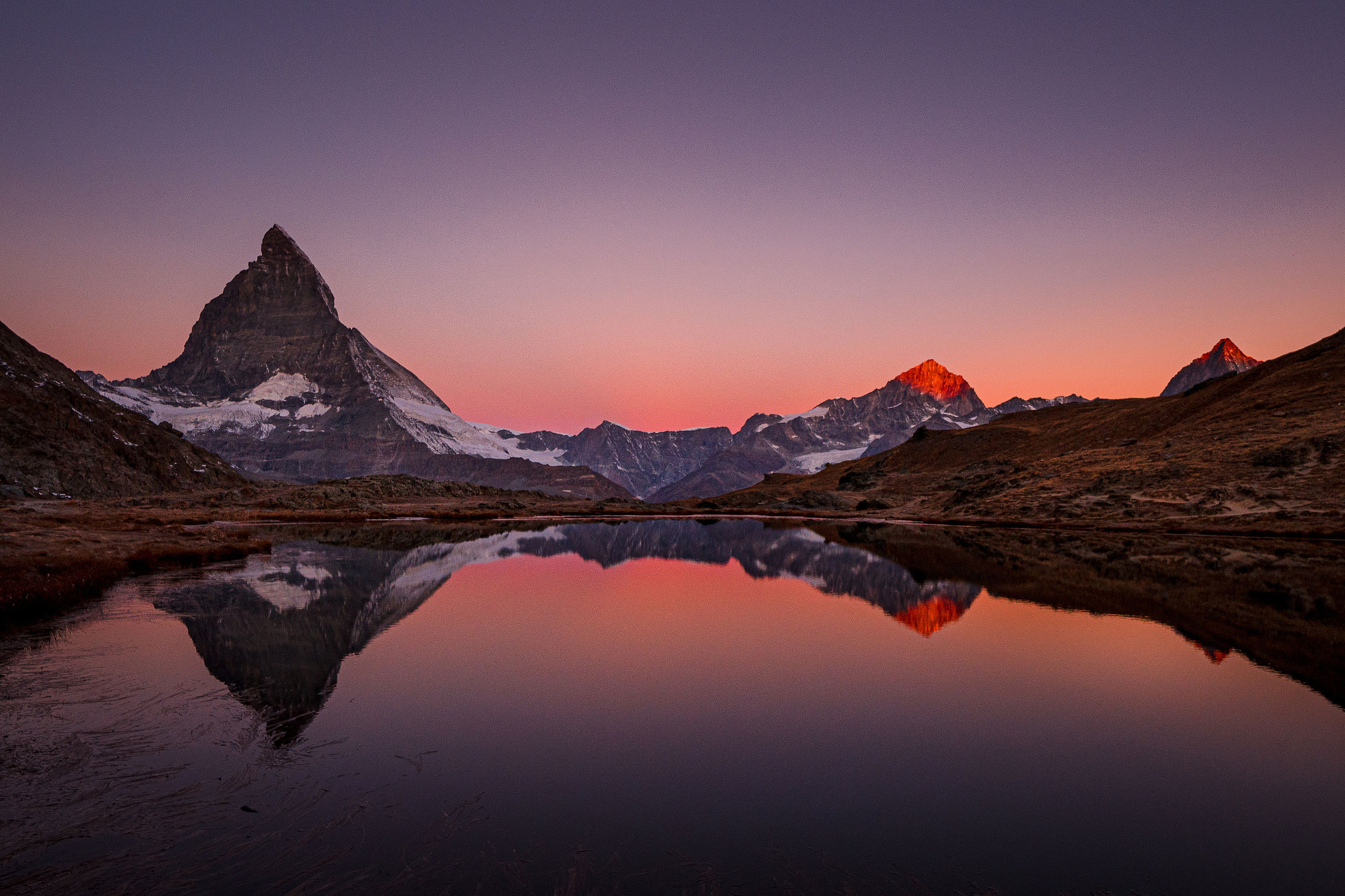 The Matterhorn is reflected in the still Riffelsee before sunrise.
