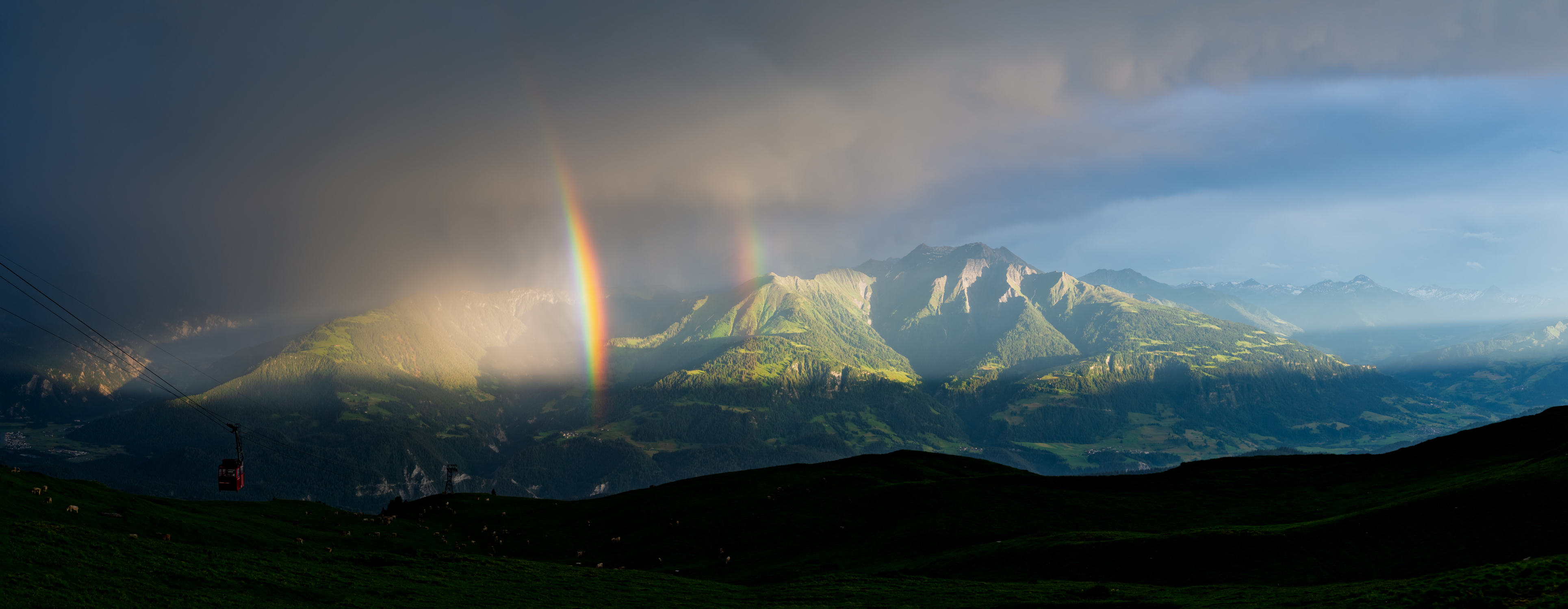 Doppelter Regenbogen über Flims vor dunklen Wolken