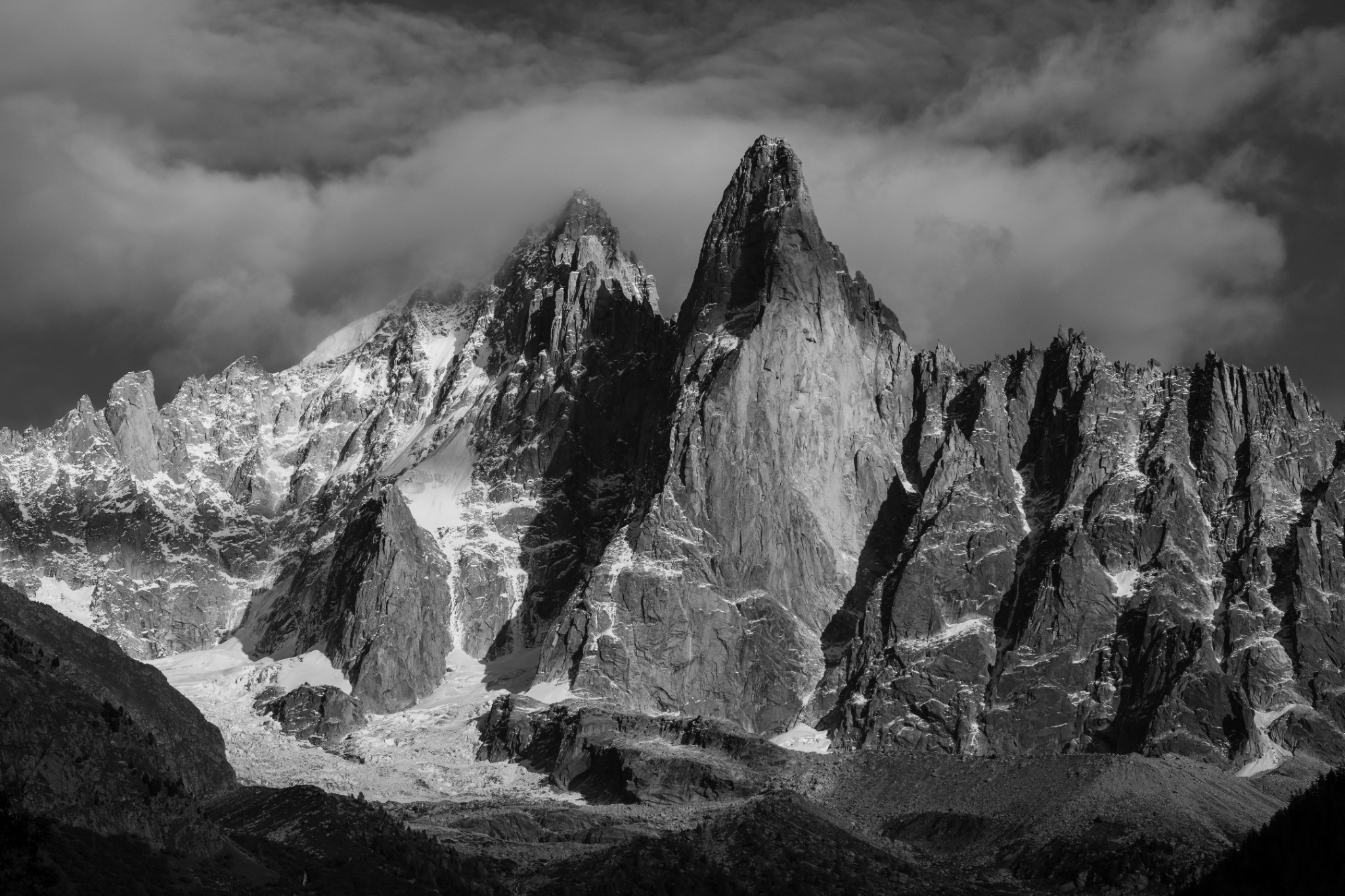 Dramatische Felsnadeln ragen in Schwarzweiss aus einer rauen, von Wolken umspielten Bergwelt.