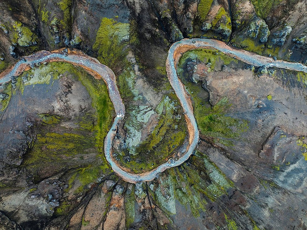 Gewundener Fluss durch dunkles Gestein mit grünen Uferflächen