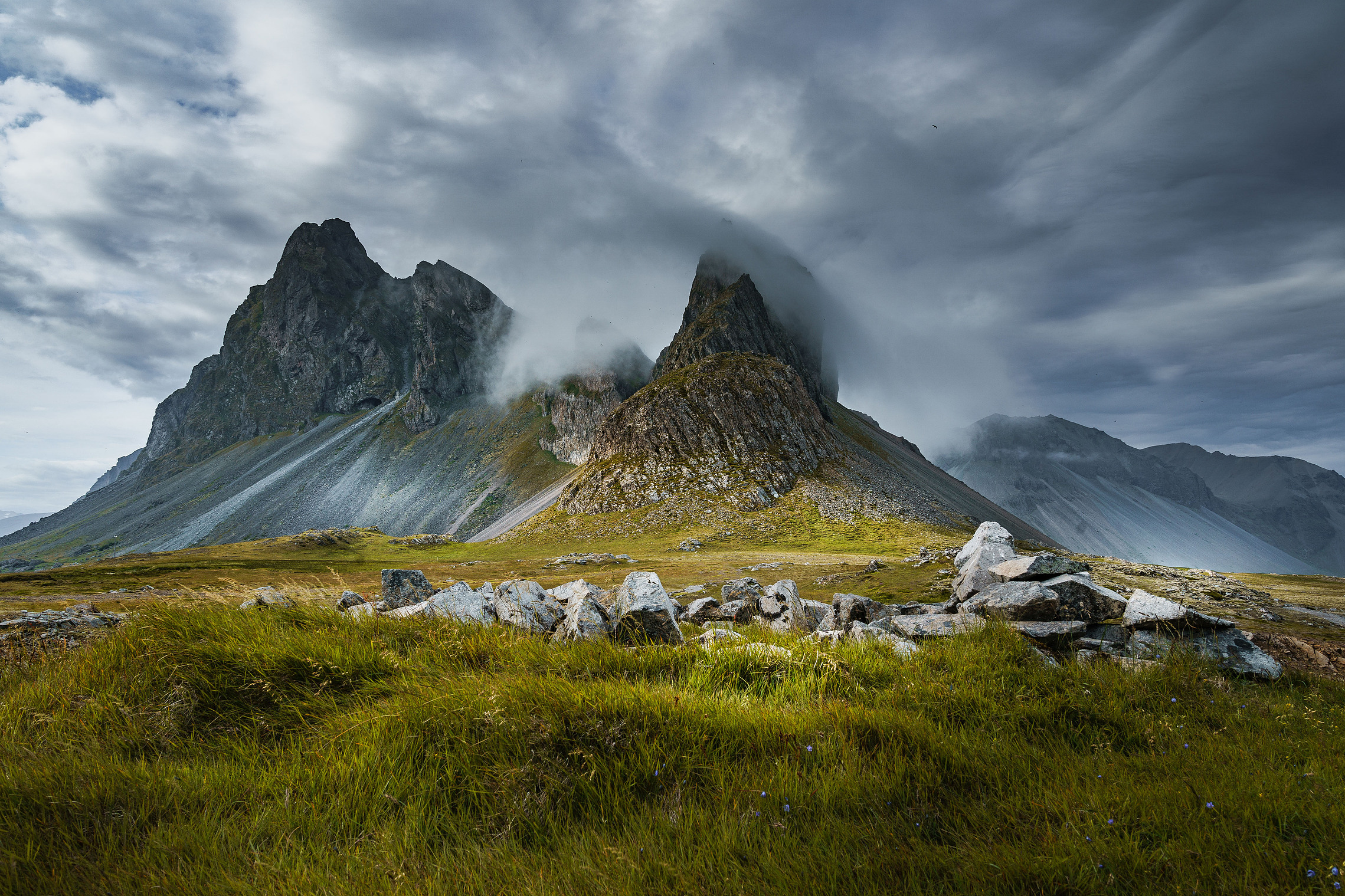 Eystrahorn under low clouds with grass and rounded boulders