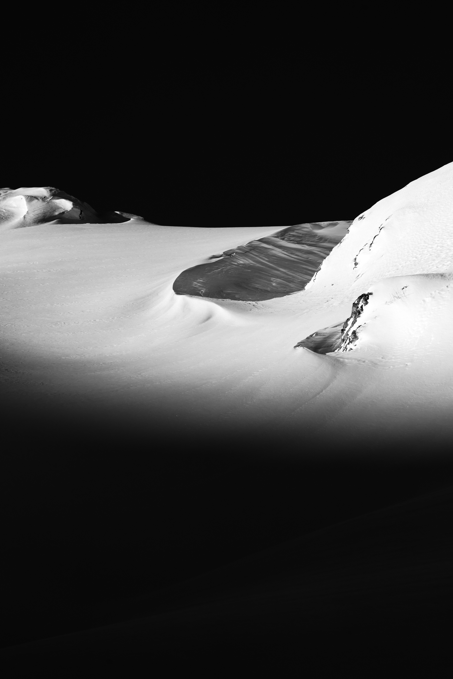 Weisse Schneefläche teilt schwarzen Bildraum mit geometrischem Schatten