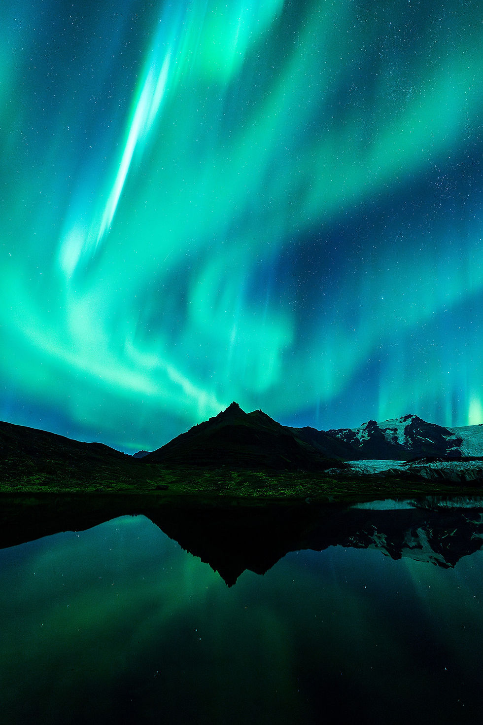 Nordlicht spiegelt sich im See hinter dunklen Bergsilhouetten