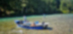 Blue-and-silver drift boat anchored in shallow water of the Skagit River, with three fly anglers wading and casting nearby against a backdrop of green forest.