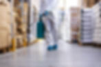 A cleaner in a protective suit air spraying a warehouse.
