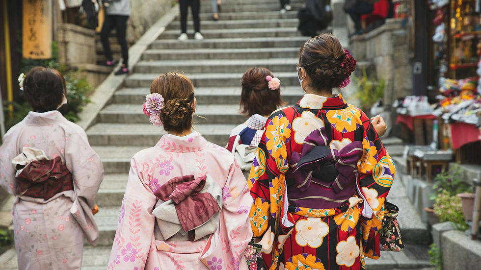 Back view of unrecognizable women with neat hairstyle in traditional kimonos walking on paved street in oriental city