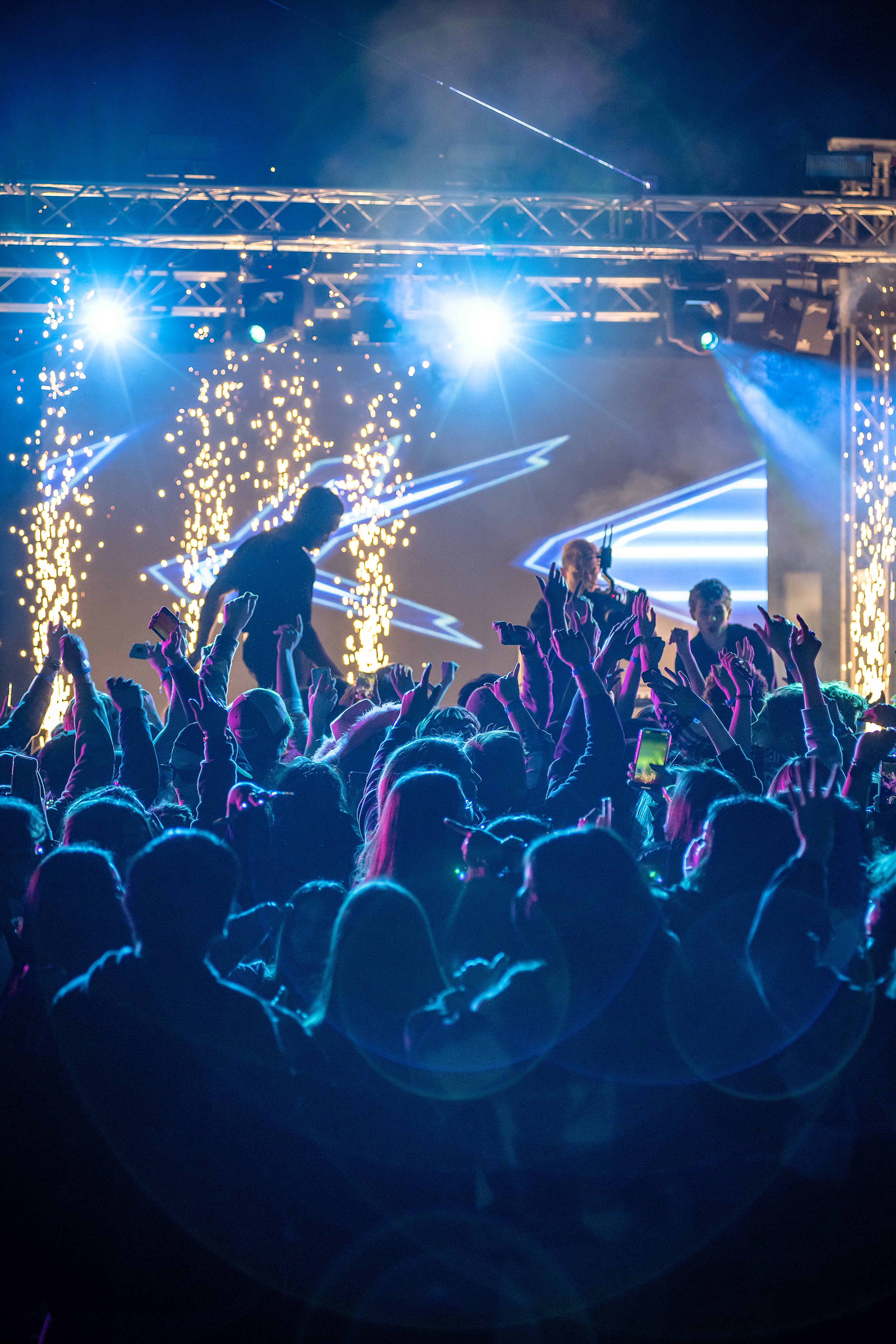 Xperience Entertainment DJs on stage at AASC State Convention, audience silhouetted with beams of light and cold sparks in background.
