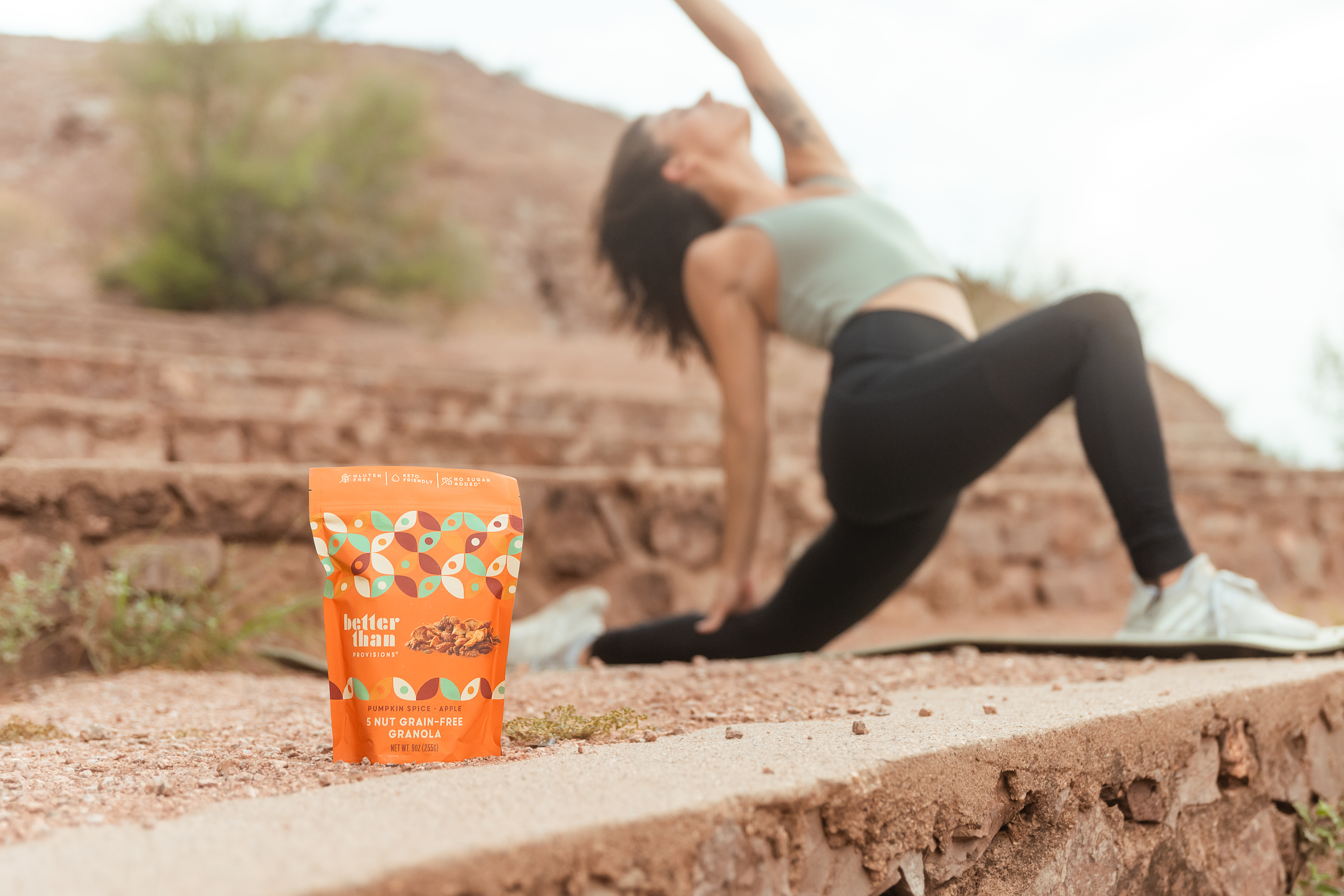 Better Than Provisions granola bag with mountain backdrop and person practicing yoga in background.
