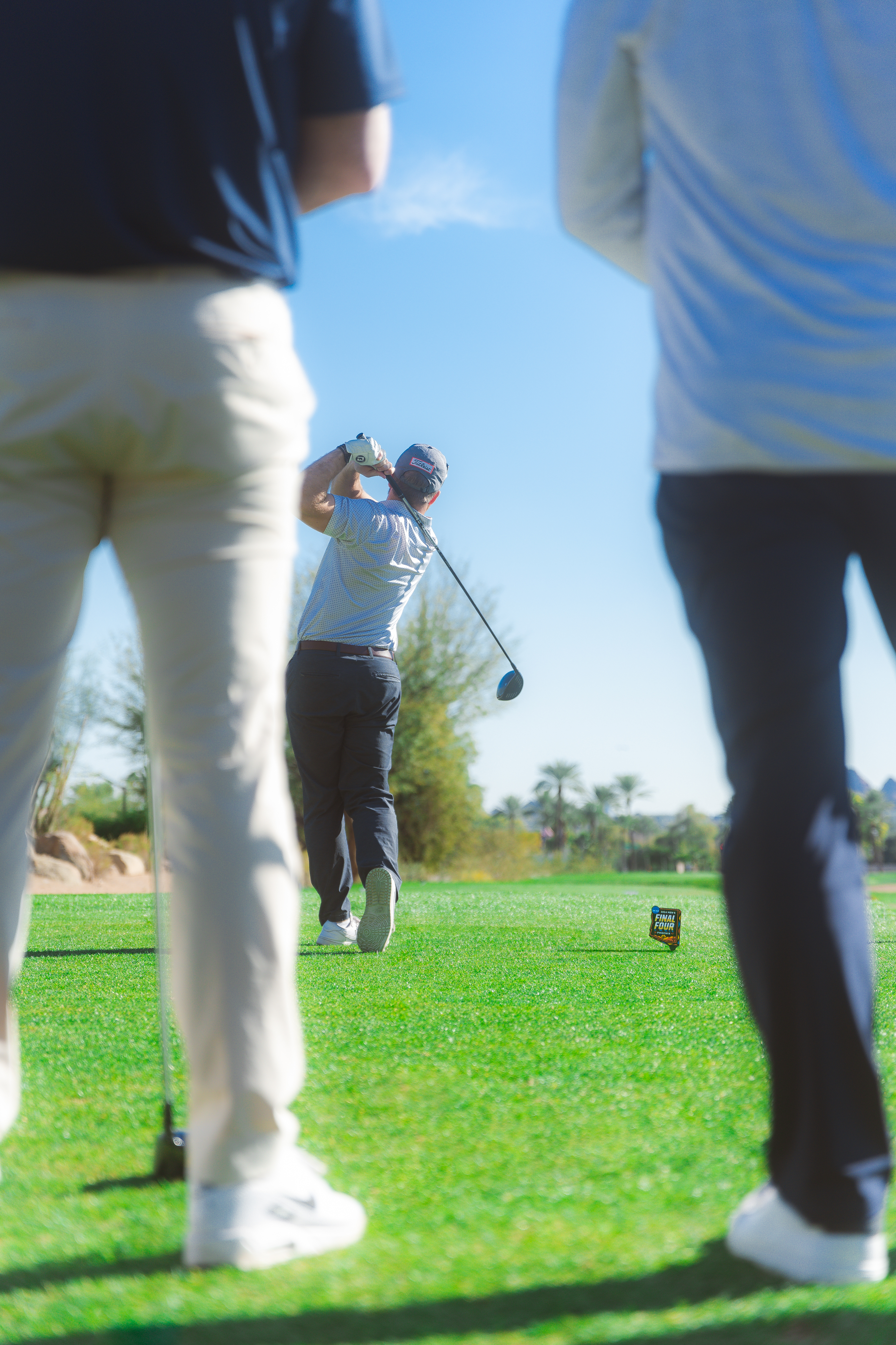 Alt Text: Golfer after hitting ball with 2024 Final Four logo flag at Phoenician golf tournament.