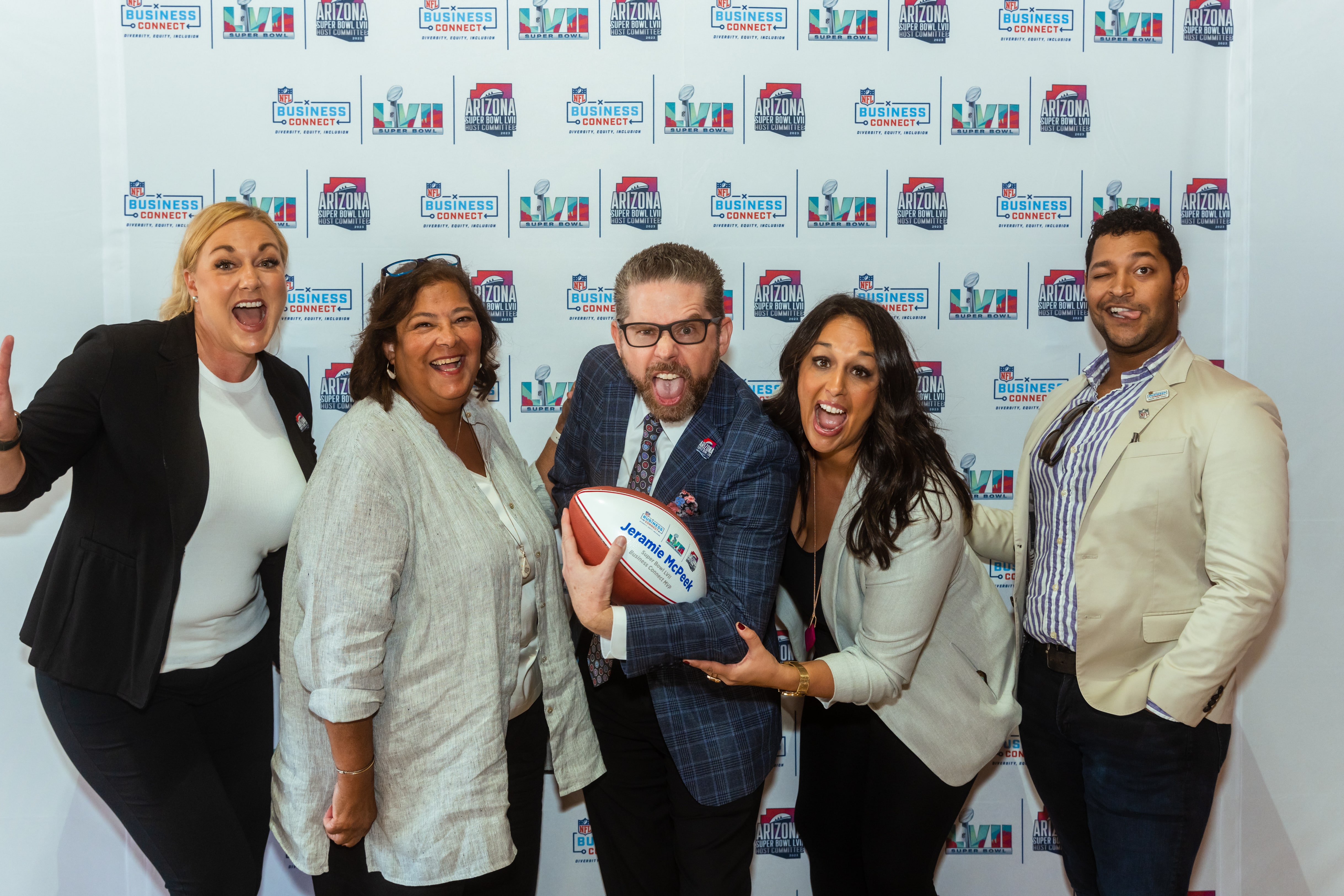 Speaker Jeramie McPeek and event team posing playfully in front of Super Bowl 57 step-and-repeat in Arizona.
