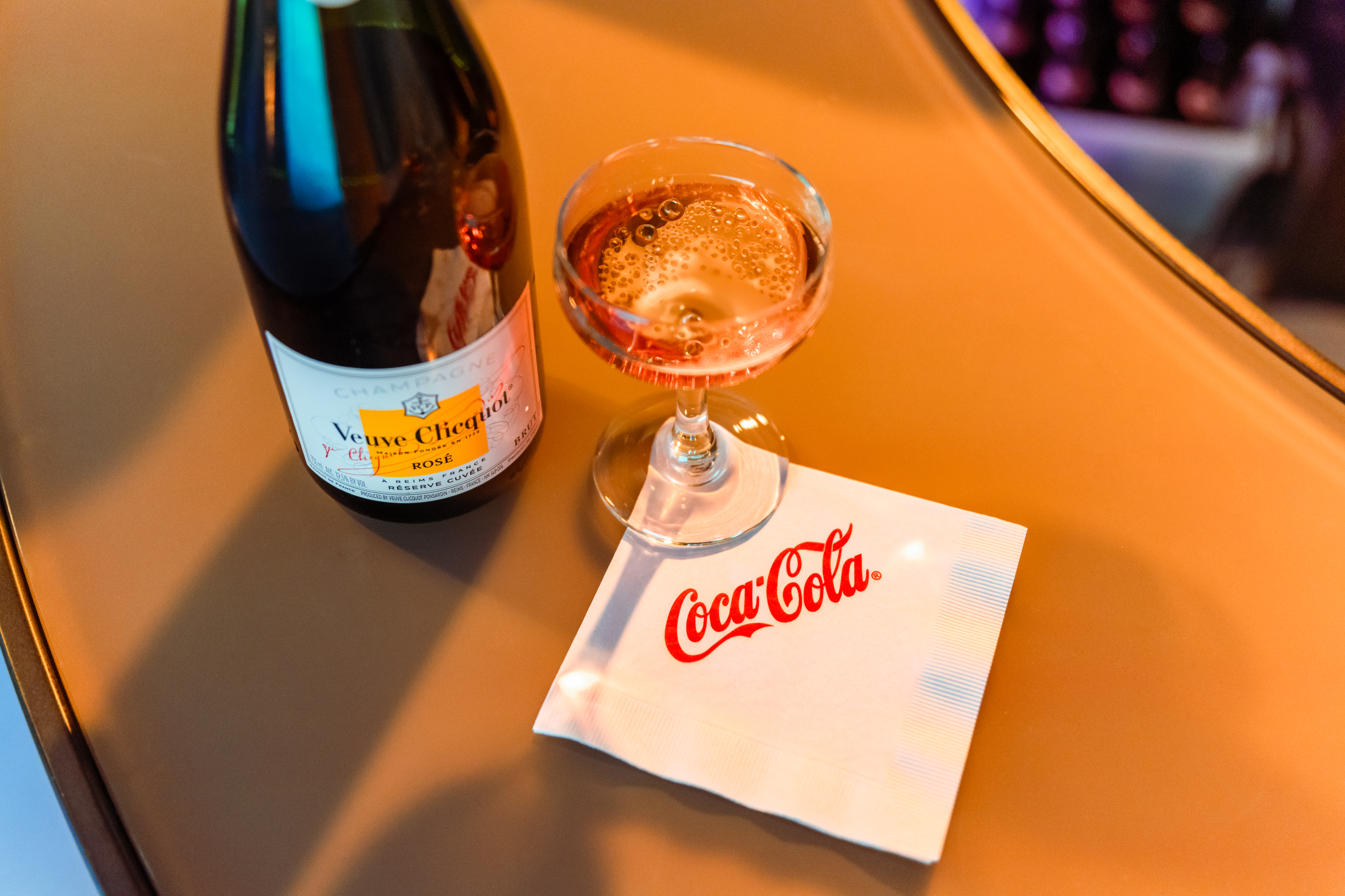 Glass of Rose with Coca-Cola logo napkin and bottle at private event bar, during Men's Final Four 2024.
