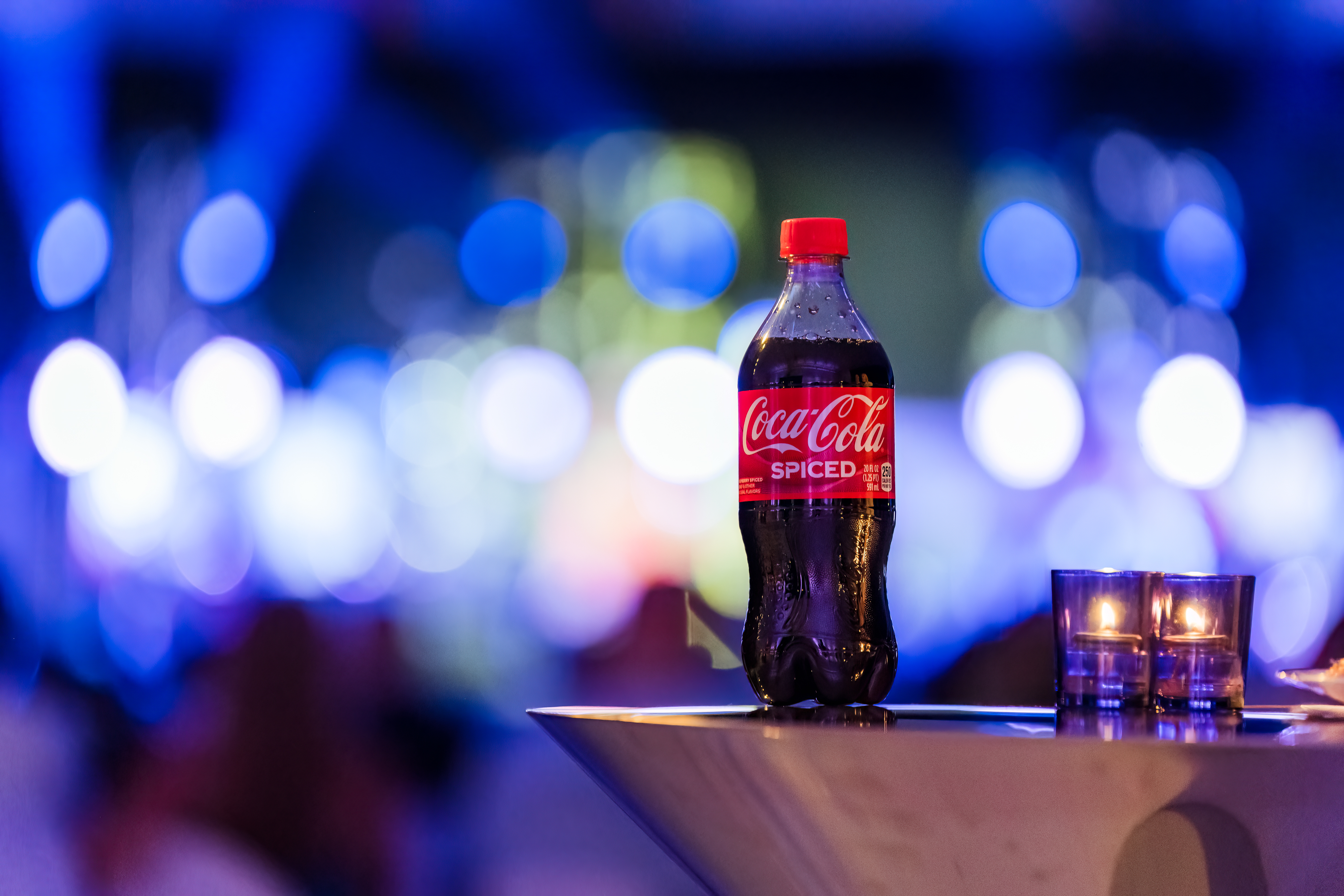SPICED Coca-Cola bottle with blurred concert background, product photography Arizona.
